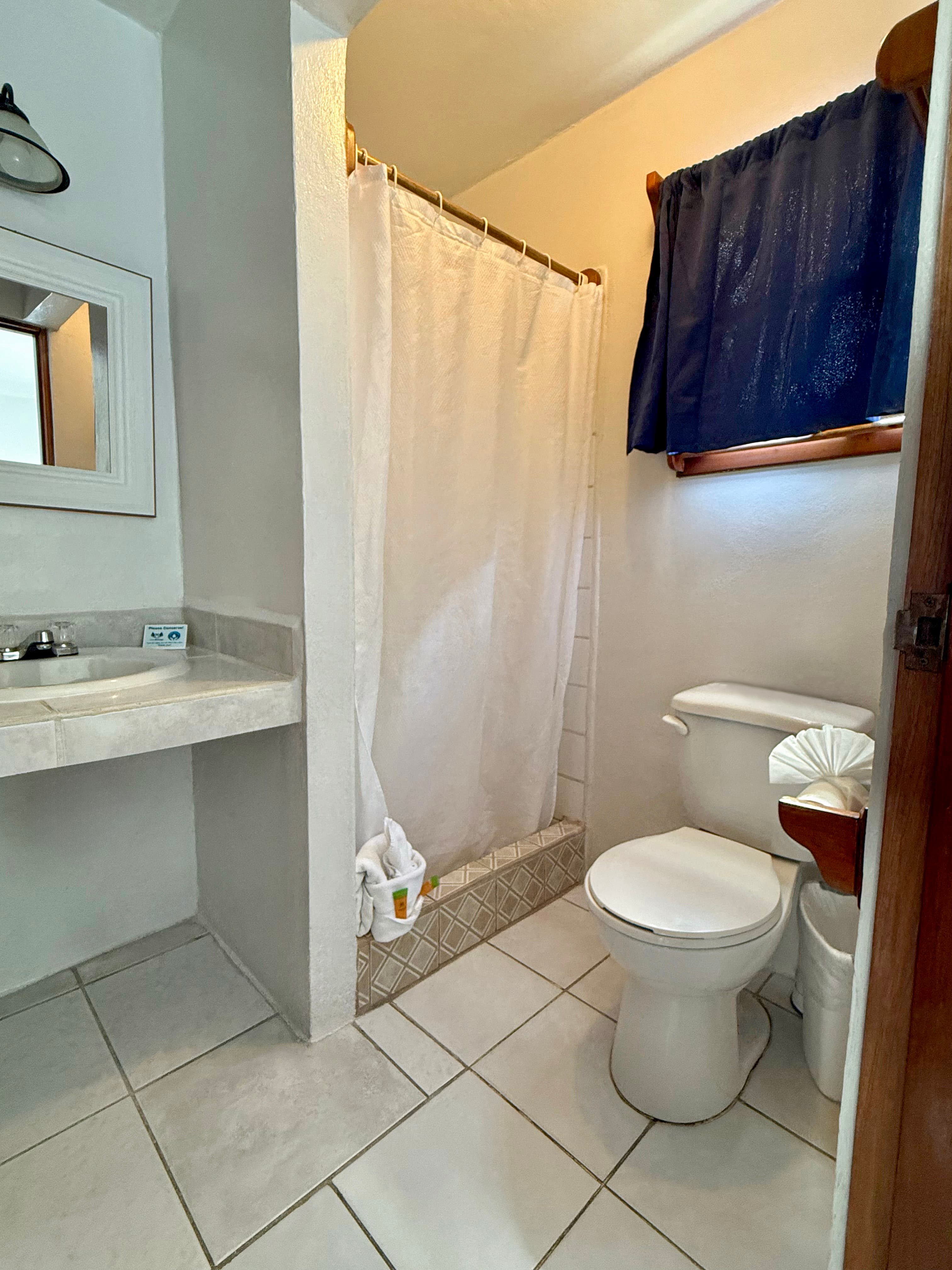 A simple and clean bathroom featuring a white toilet, a shower with a white curtain, and a vanity with a sink and mirror.
