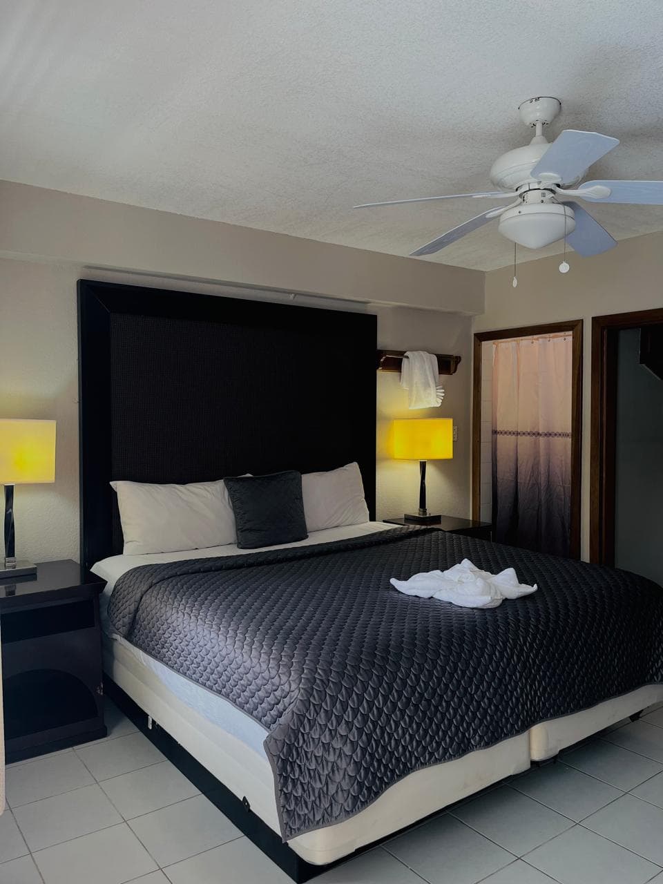 A well-appointed bedroom with a king-size bed, dark gray bedding, nightstands with lamps, and a ceiling fan for comfort.