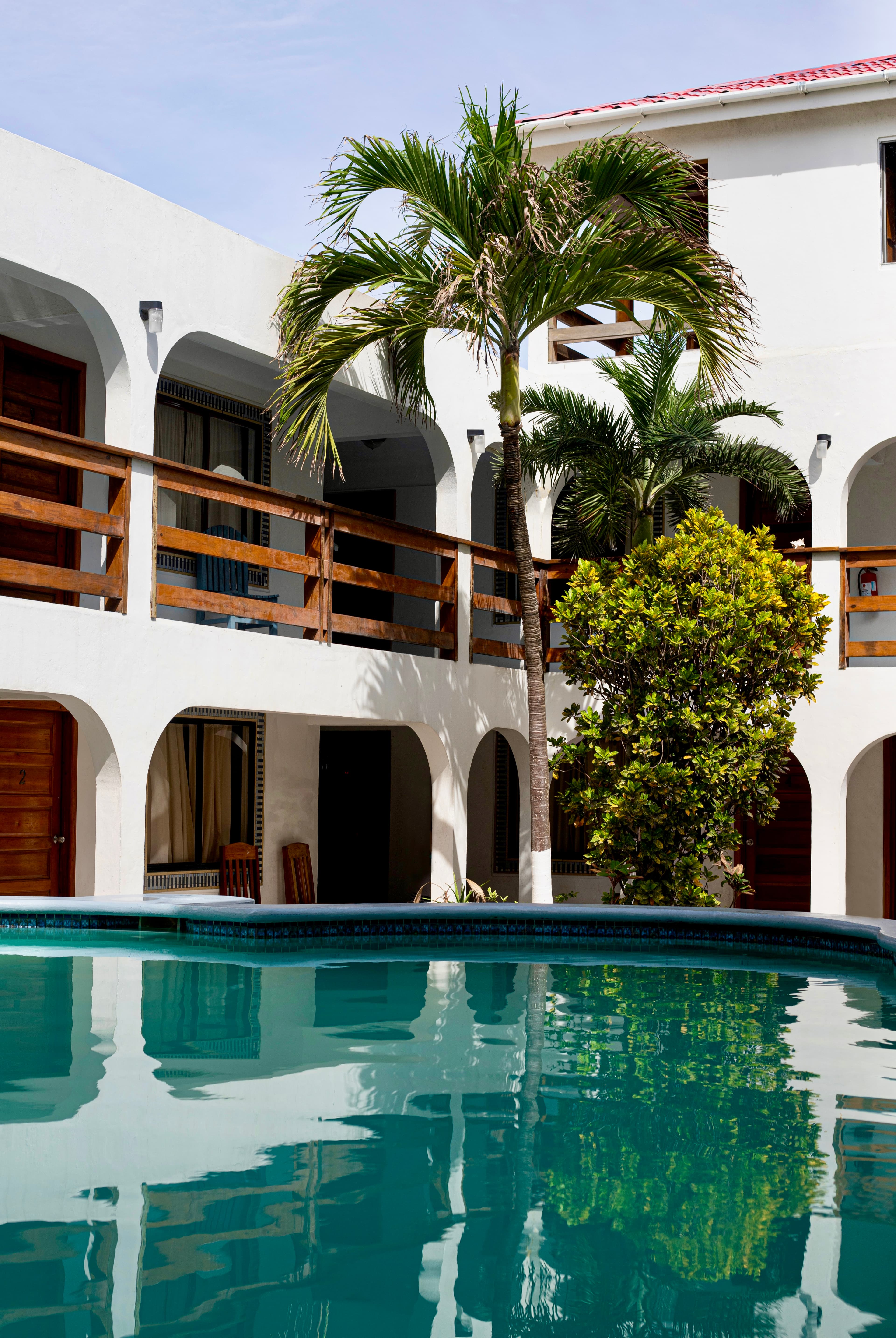 A beautiful resort with white archways and wooden railings surrounds a sparkling turquoise pool, with palm trees adding to the tropical ambiance.