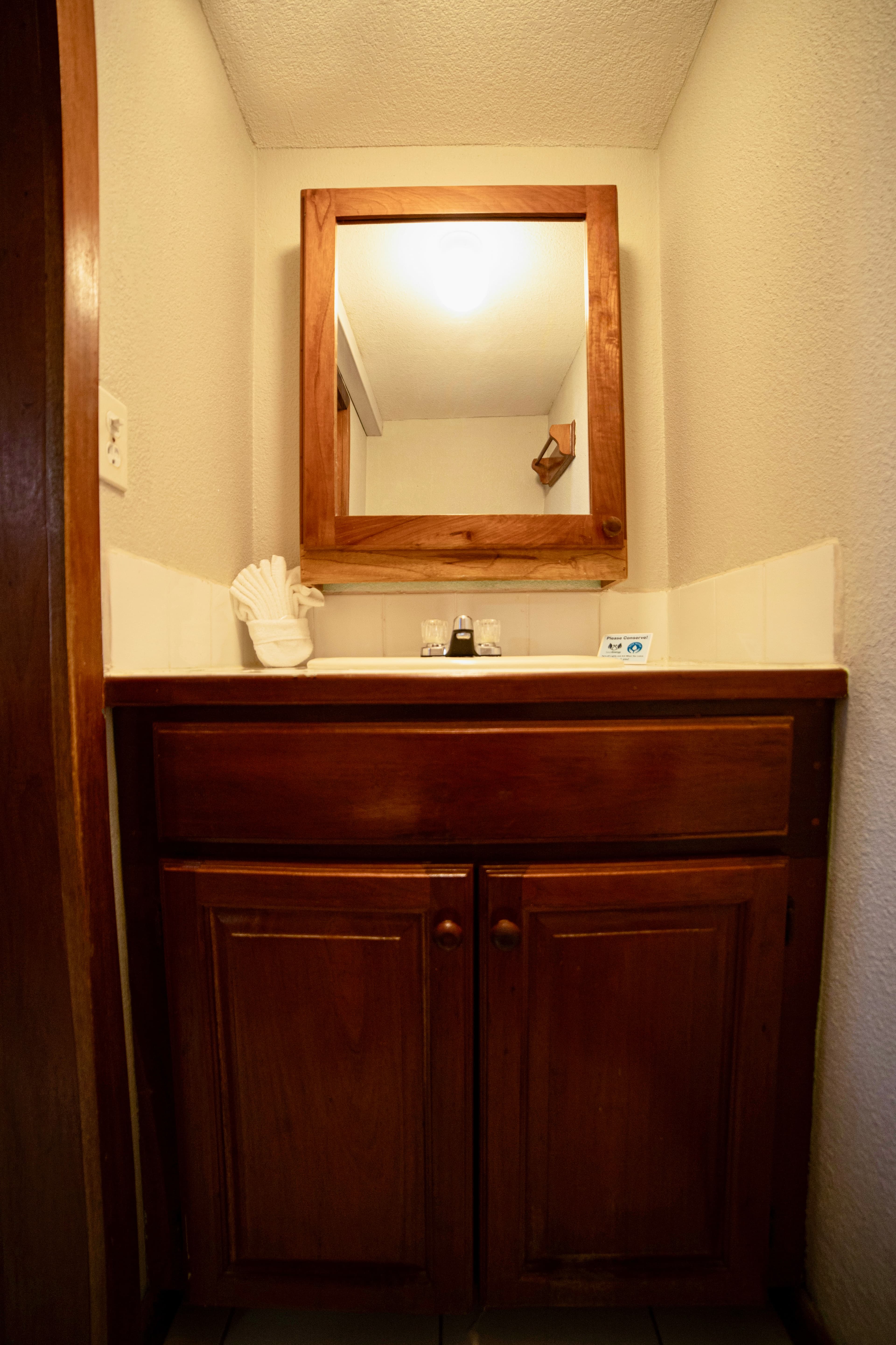 A compact bathroom vanity featuring a wooden cabinet with a white countertop and a mirror with a wooden frame above the sink.