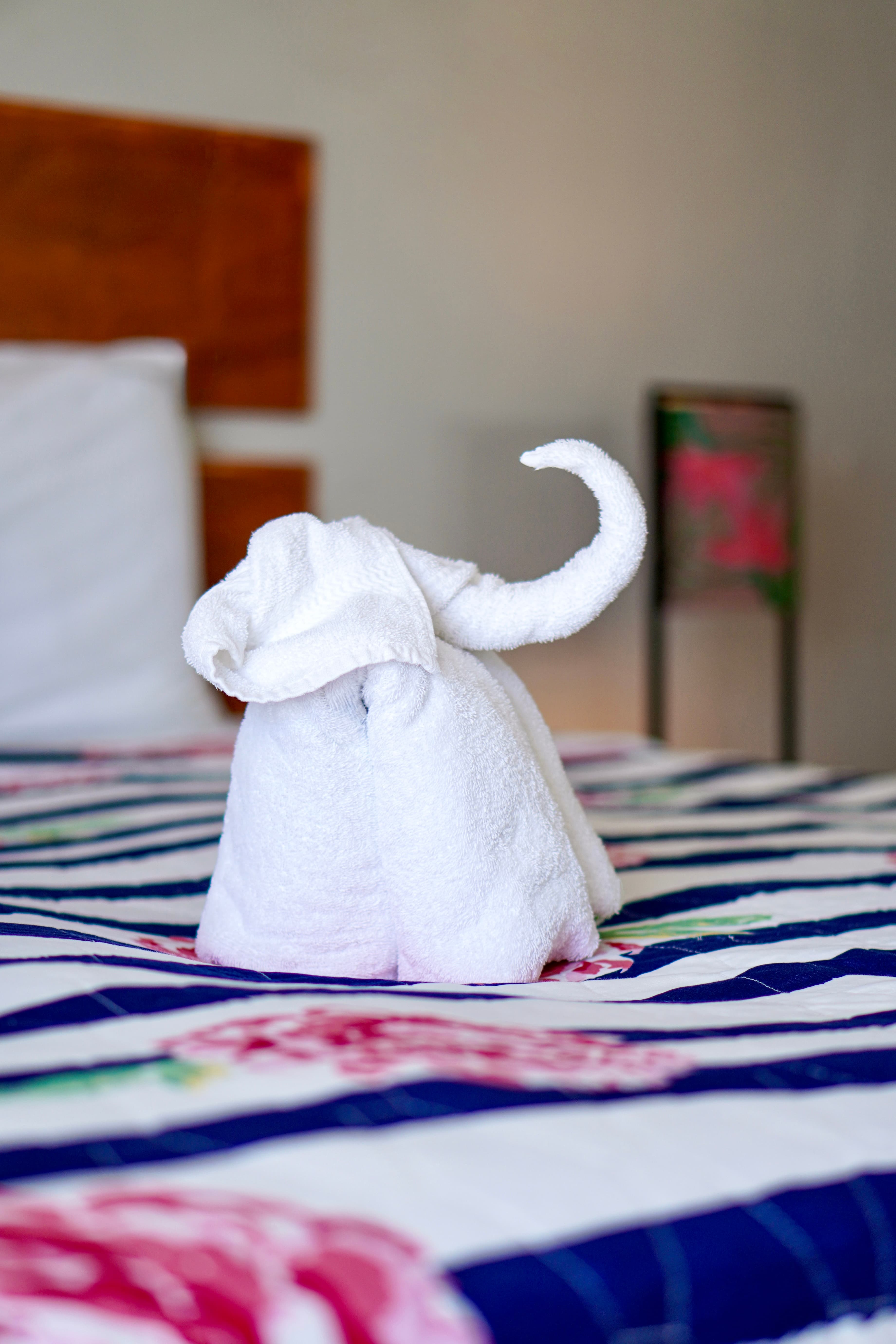 A cute white towel elephant sits on a bed with a colorful striped and floral patterned blanket, adding a playful touch.