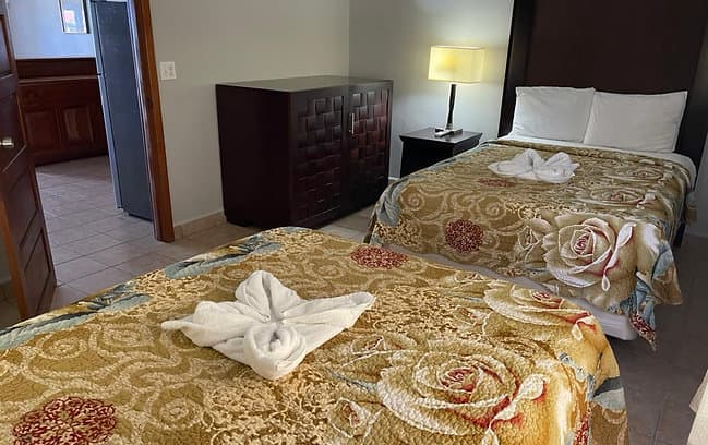 A welcoming hotel room with two beds, golden floral bedspreads, creatively folded towels, and a bedside table with a lamp