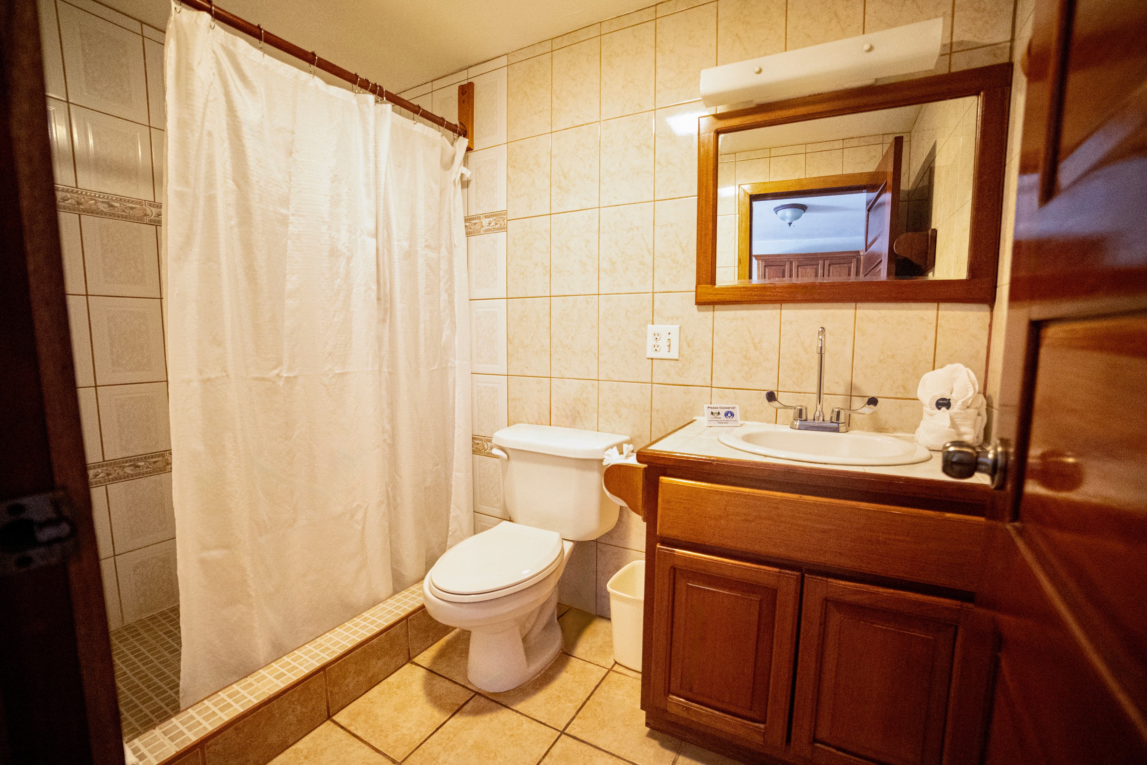 A compact bathroom featuring a shower with a white curtain, a toilet, and a wooden vanity with a sink and mirror.