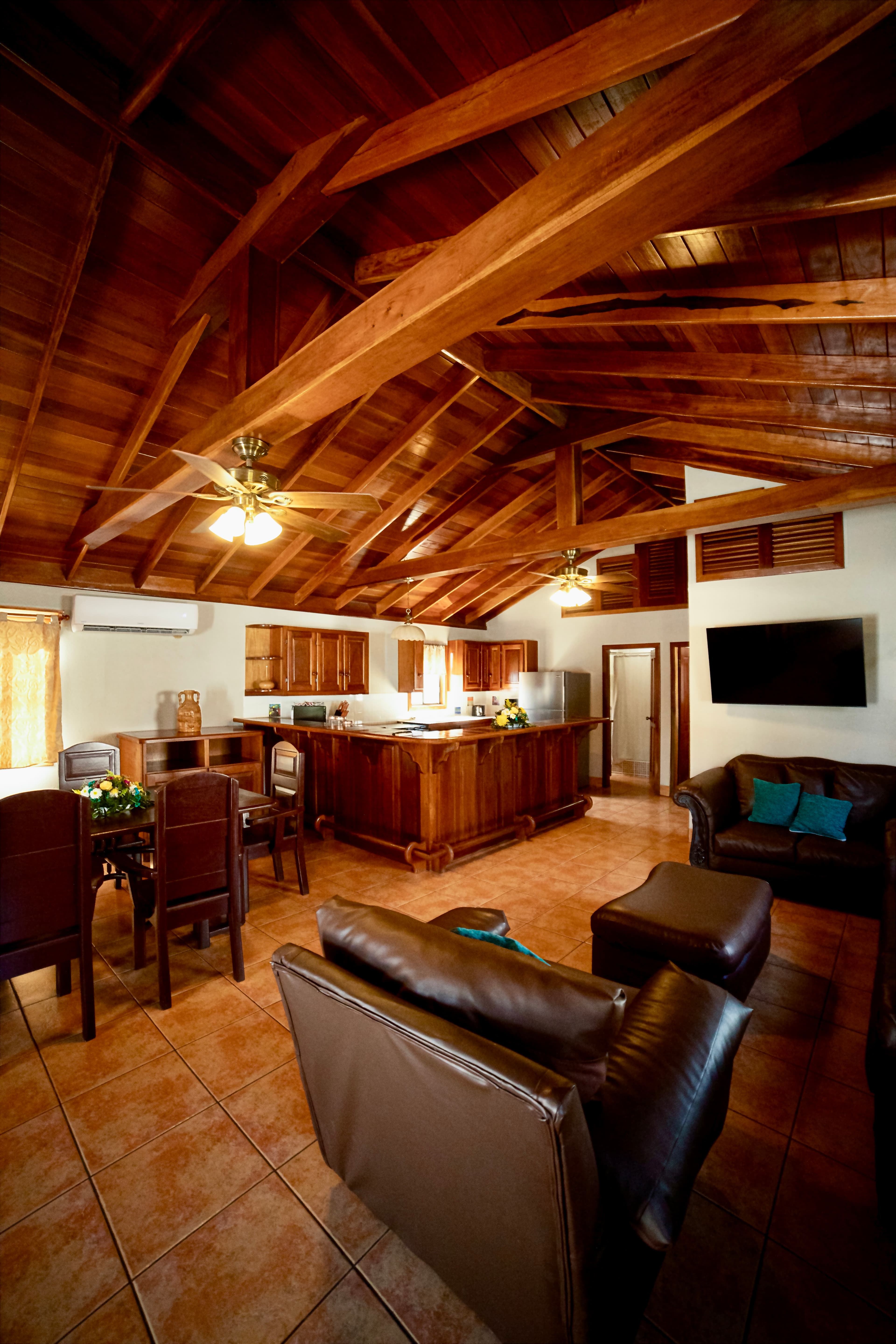 A grand living space with high vaulted wooden ceilings, an open-concept kitchen with a large bar, and a comfortable lounge area.