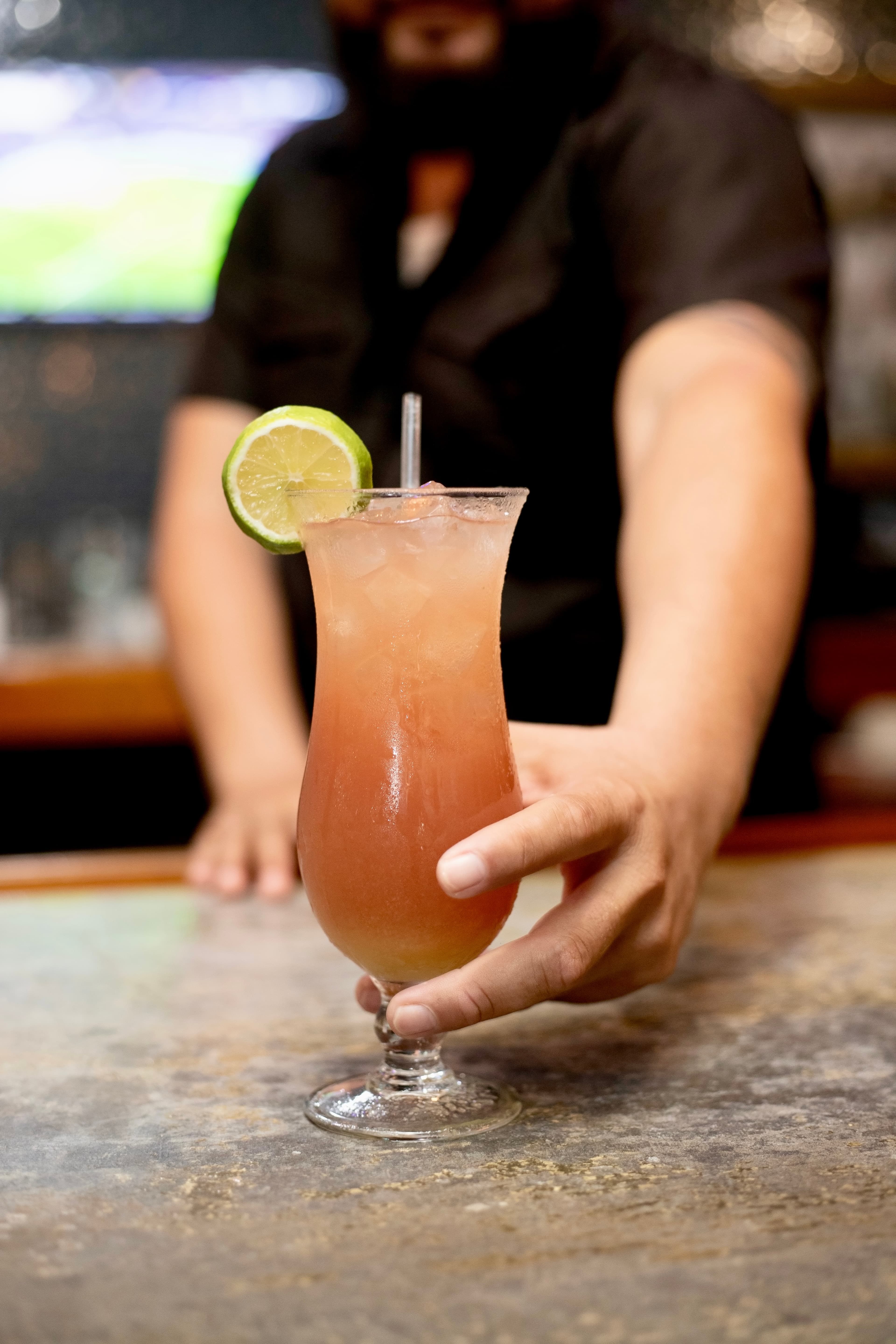 A bartender serves a cocktail with a lime garnish at a bar.