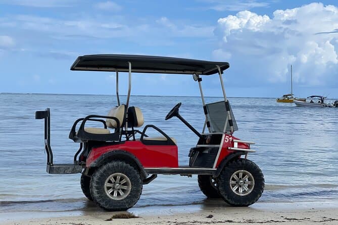 A red golf cart with large tires parked by the water's edge under a blue sky.