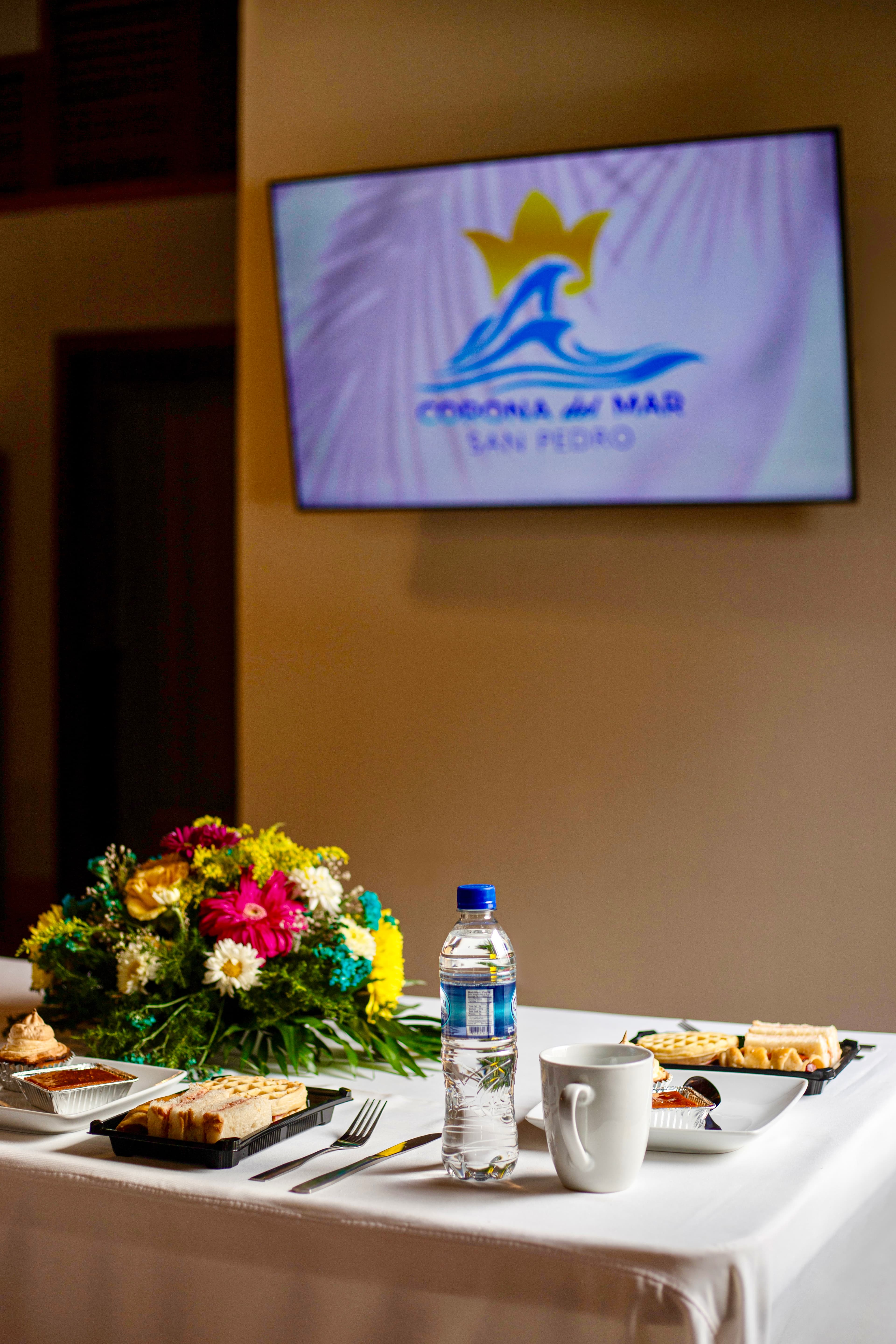 Table set with food, a water bottle, and a floral arrangement in front of a screen displaying a logo.