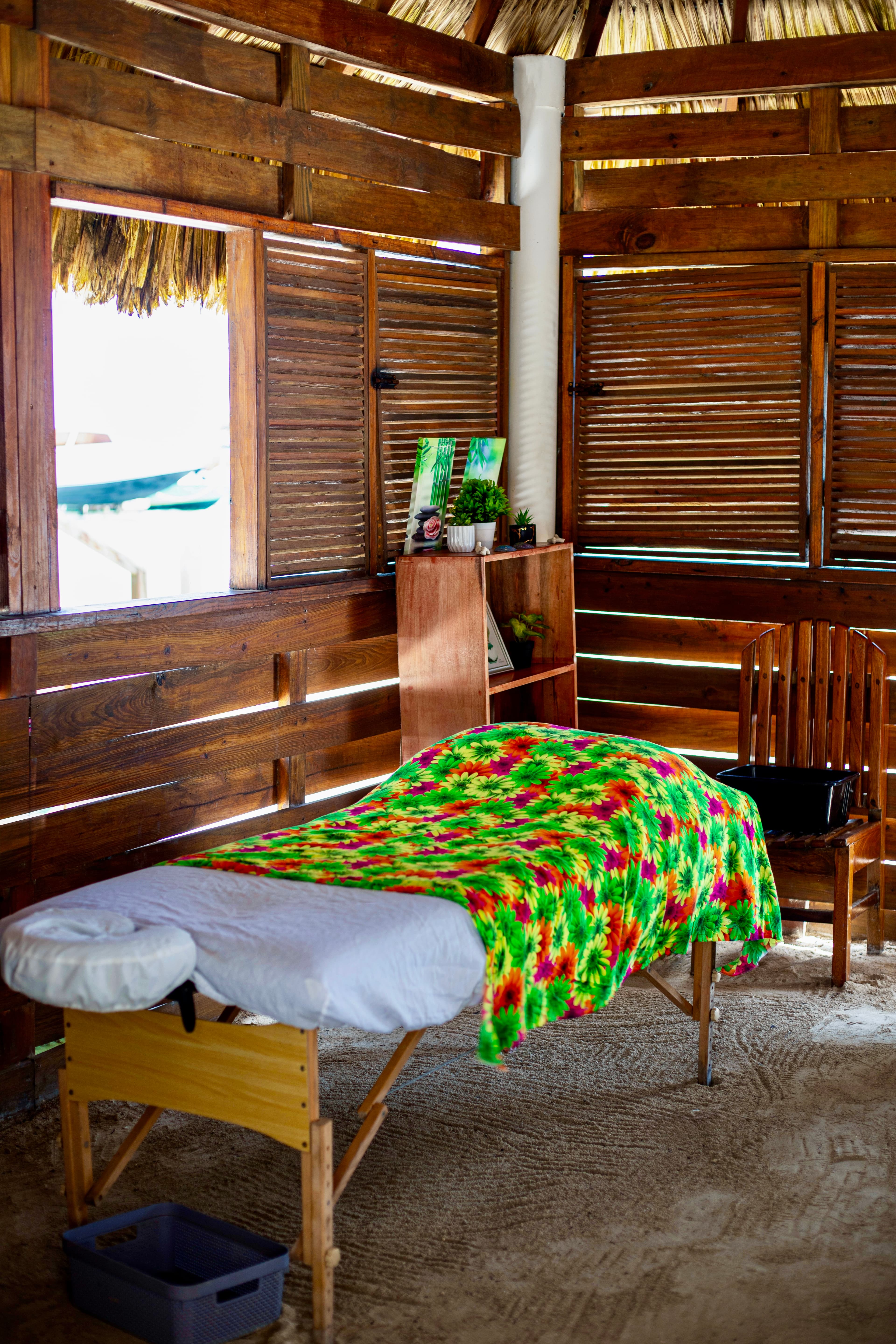 A colorful massage table in a wooden hut with natural light streaming through slatted walls.