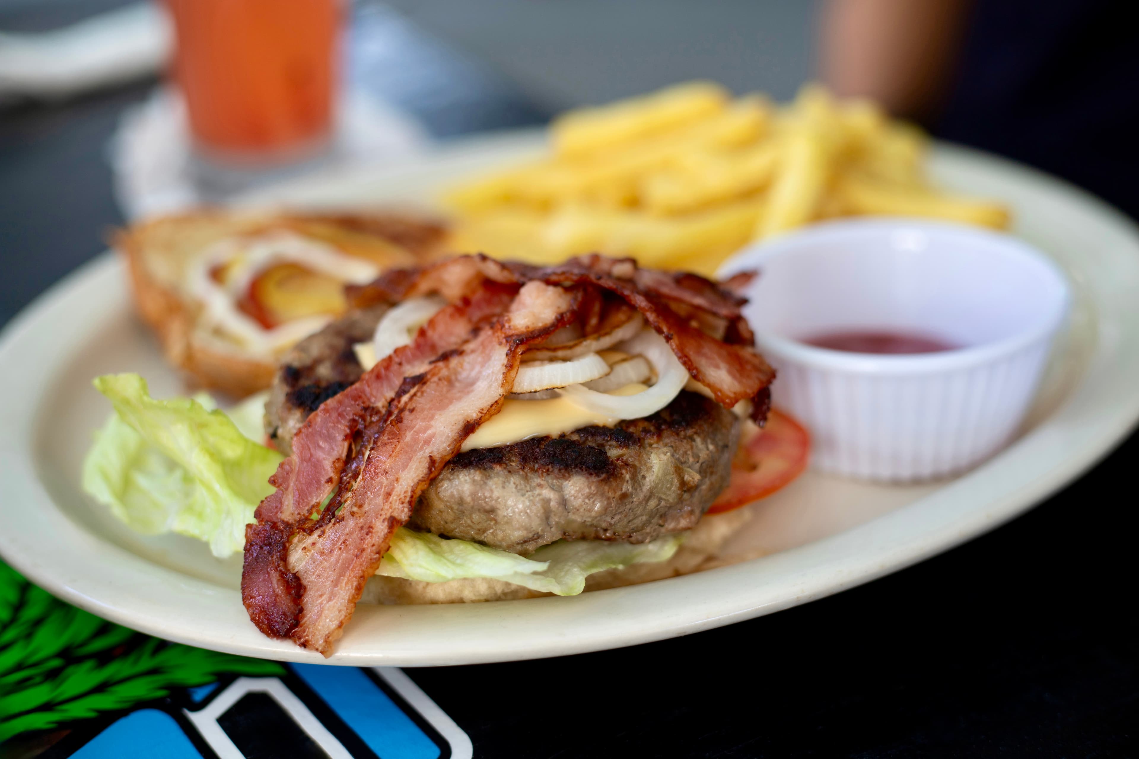 A bacon cheeseburger with lettuce, tomato, onions, and a side of fries.