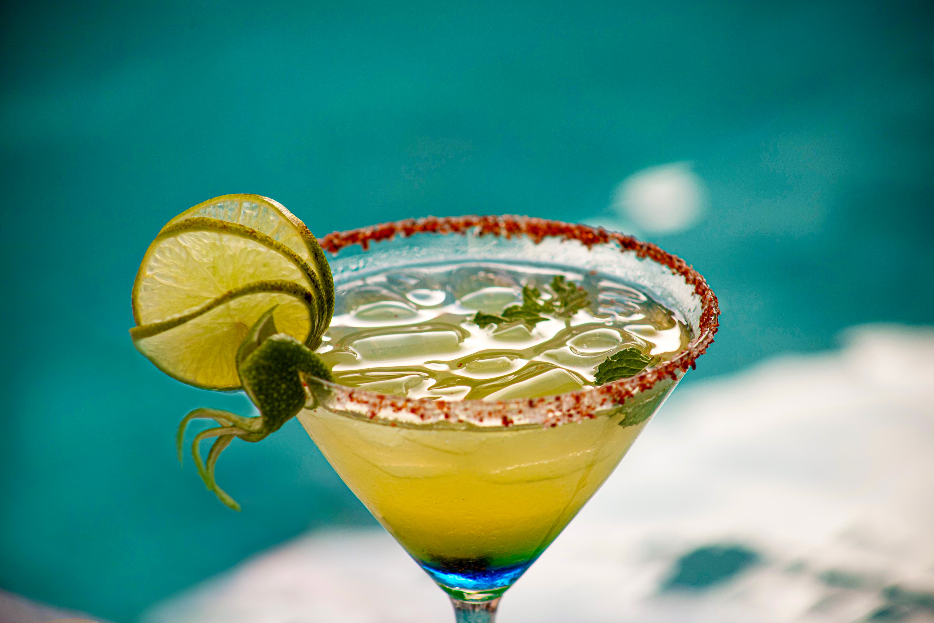A close-up of a margarita with lime garnishes and a salt rim, against a blue background.