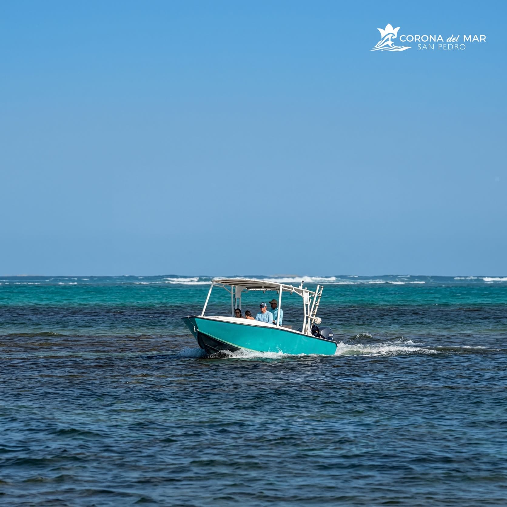 A turquoise boat carrying four people navigates through a calm turquoise sea.